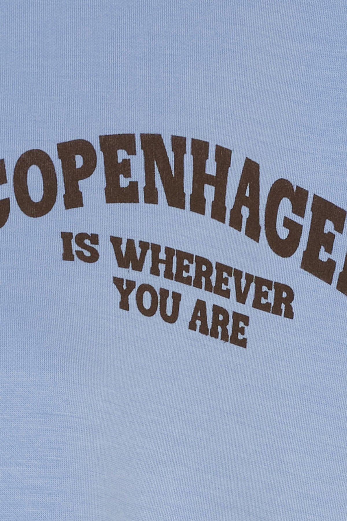 Lyseblå t-shirt med brun tekst "Copenhagen is wherever you are" i buet design.
