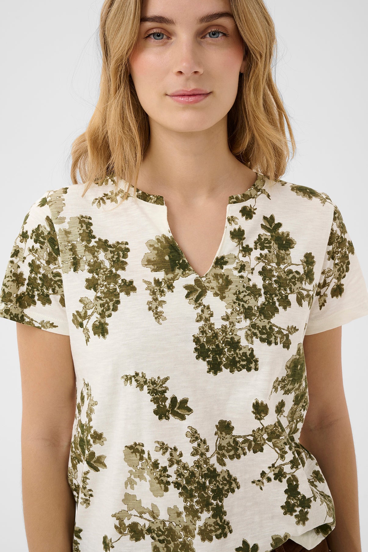 Kortærmet hvid bluse med olivengrønt blomsterprint og V-udskæring.