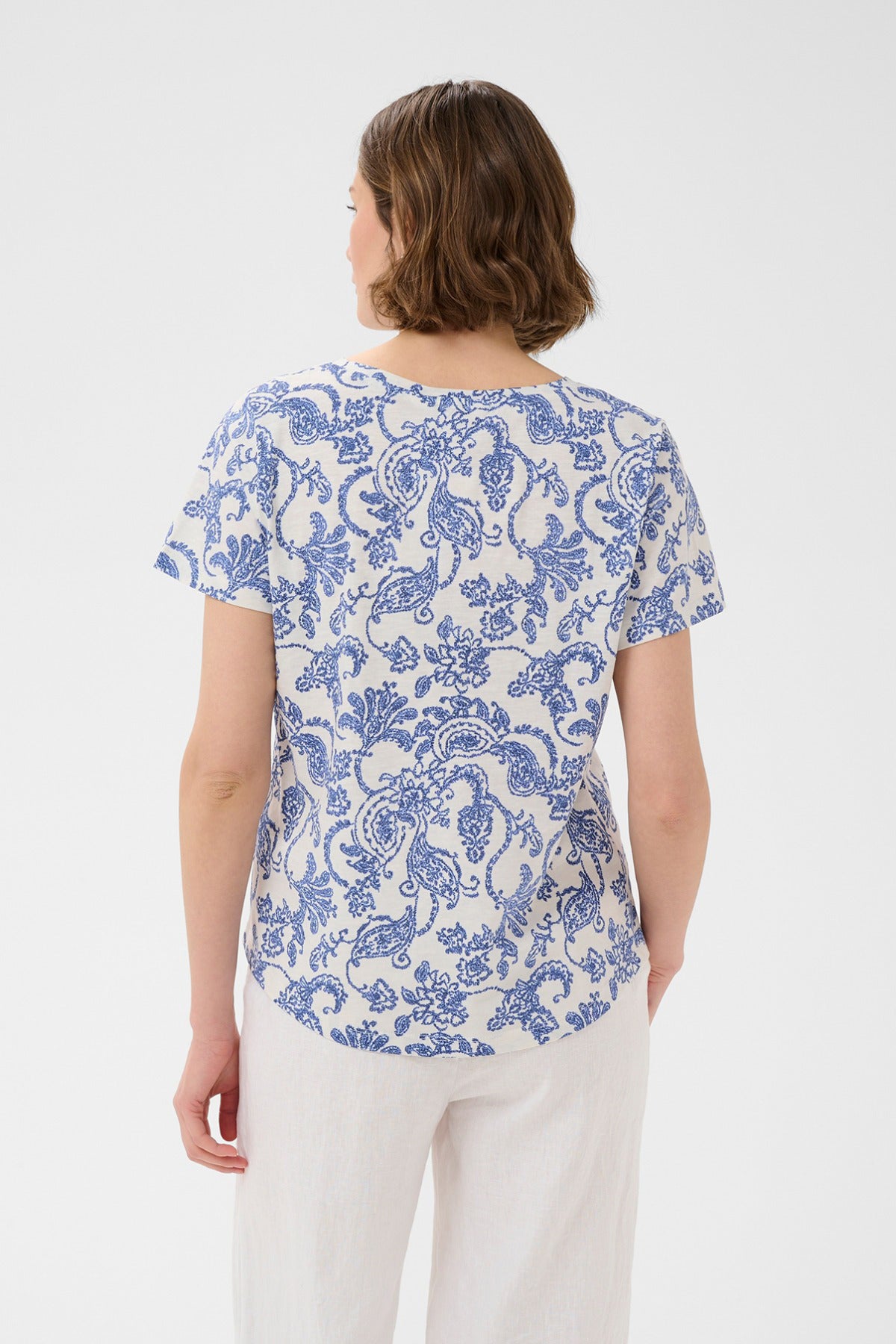 Kortærmet bluse med hvid bund og blå paisley-blomsterprint, rund hals og løs pasform.