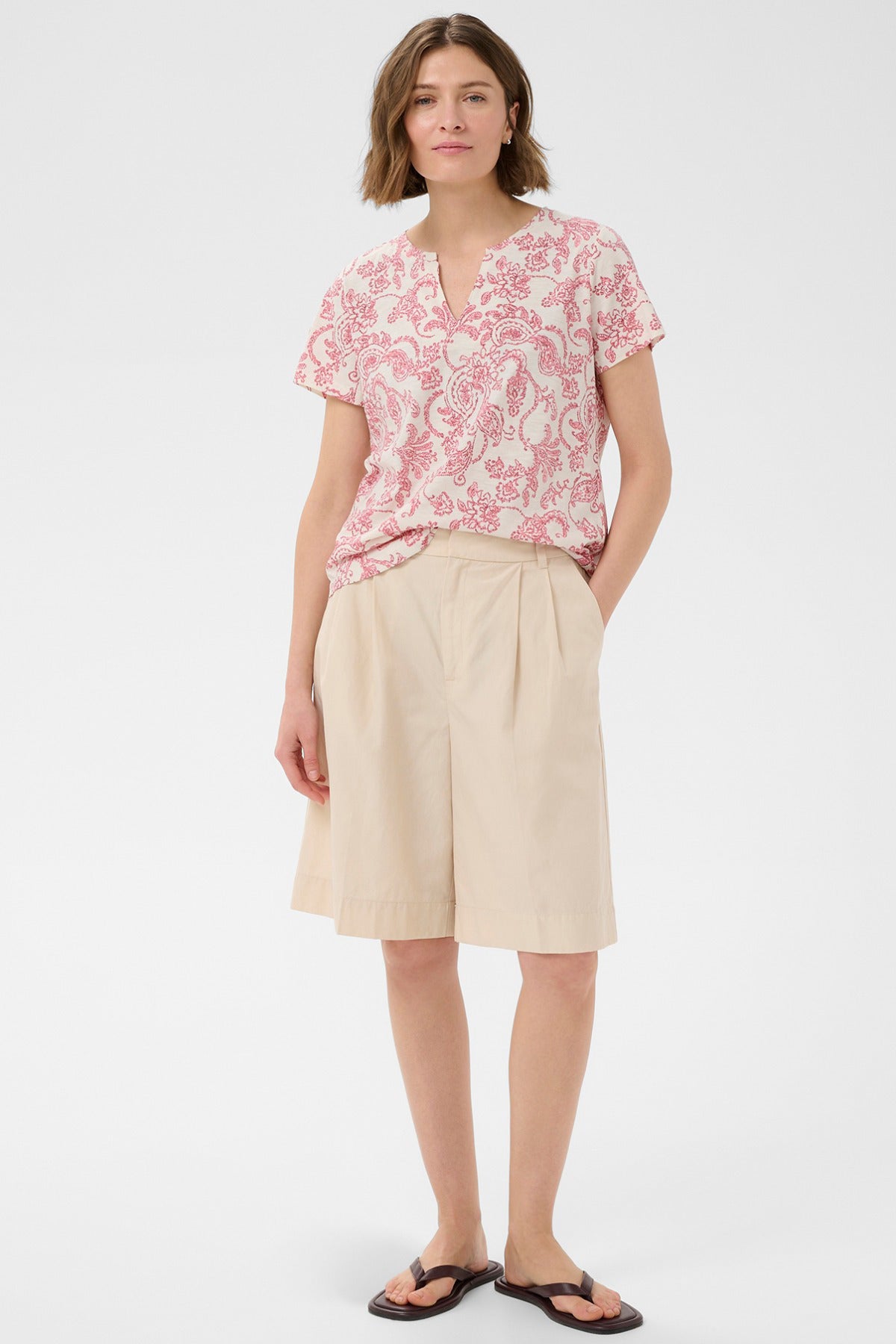 Kortærmet bluse med pink blomsterprint og v-hals, stylet med beige knælange shorts.