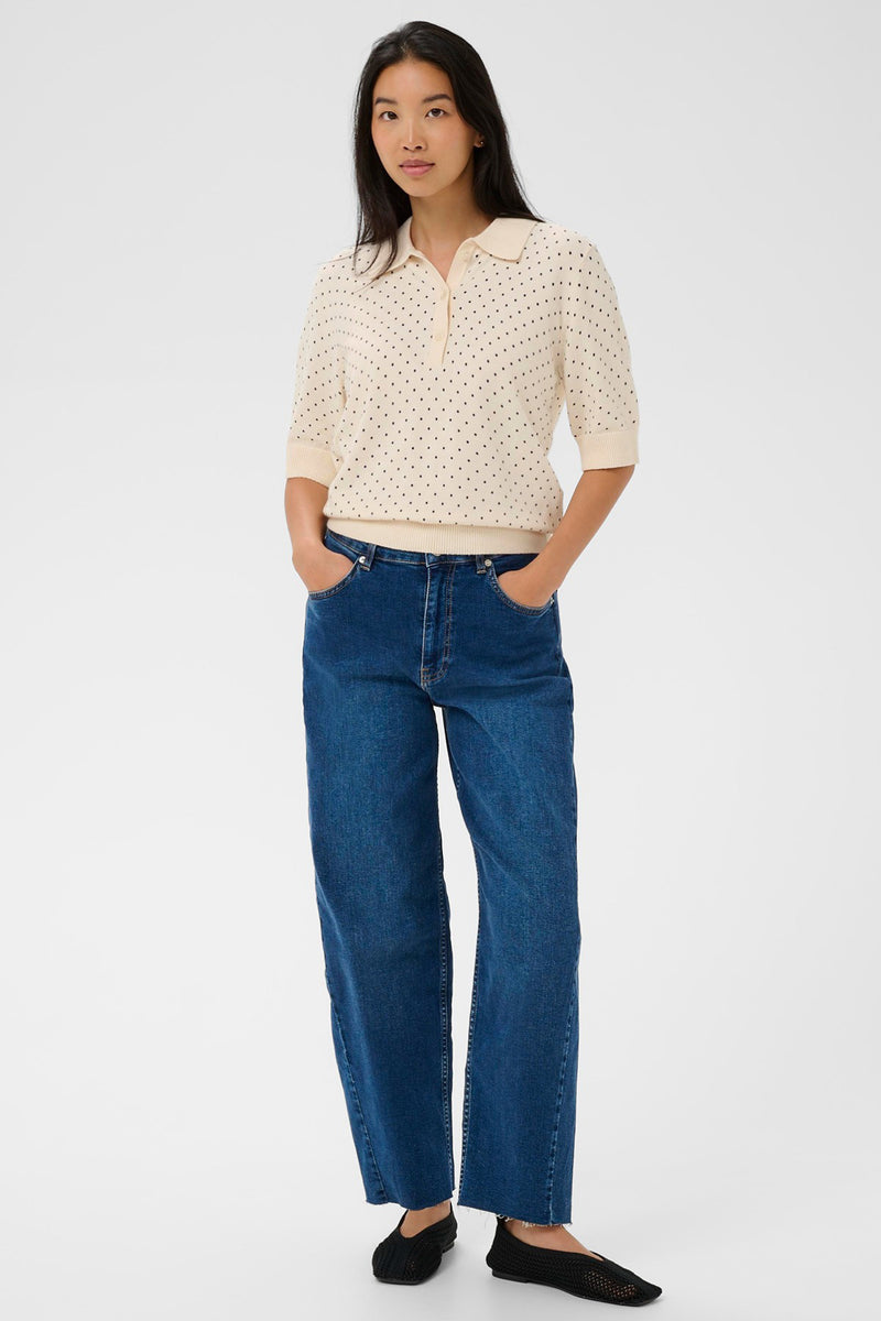 Kremfarvet pikéskjorte med lysebrune prikker og korte ærmer kombineret med mørkeblå jeans og sorte flade sko.
