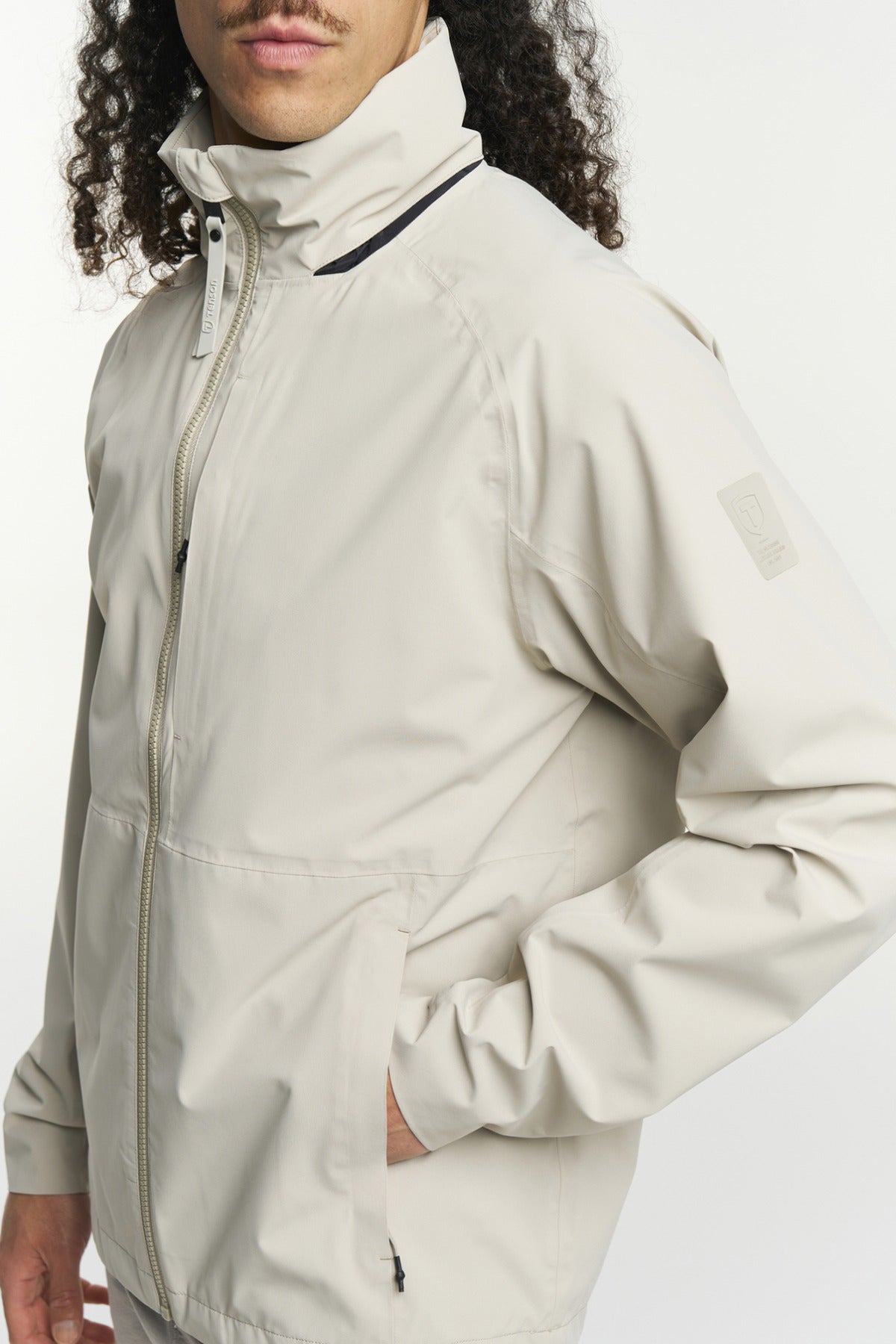 Beige funktionel skaljakke med høj krave, lynlås og sidelommer i sporty design.