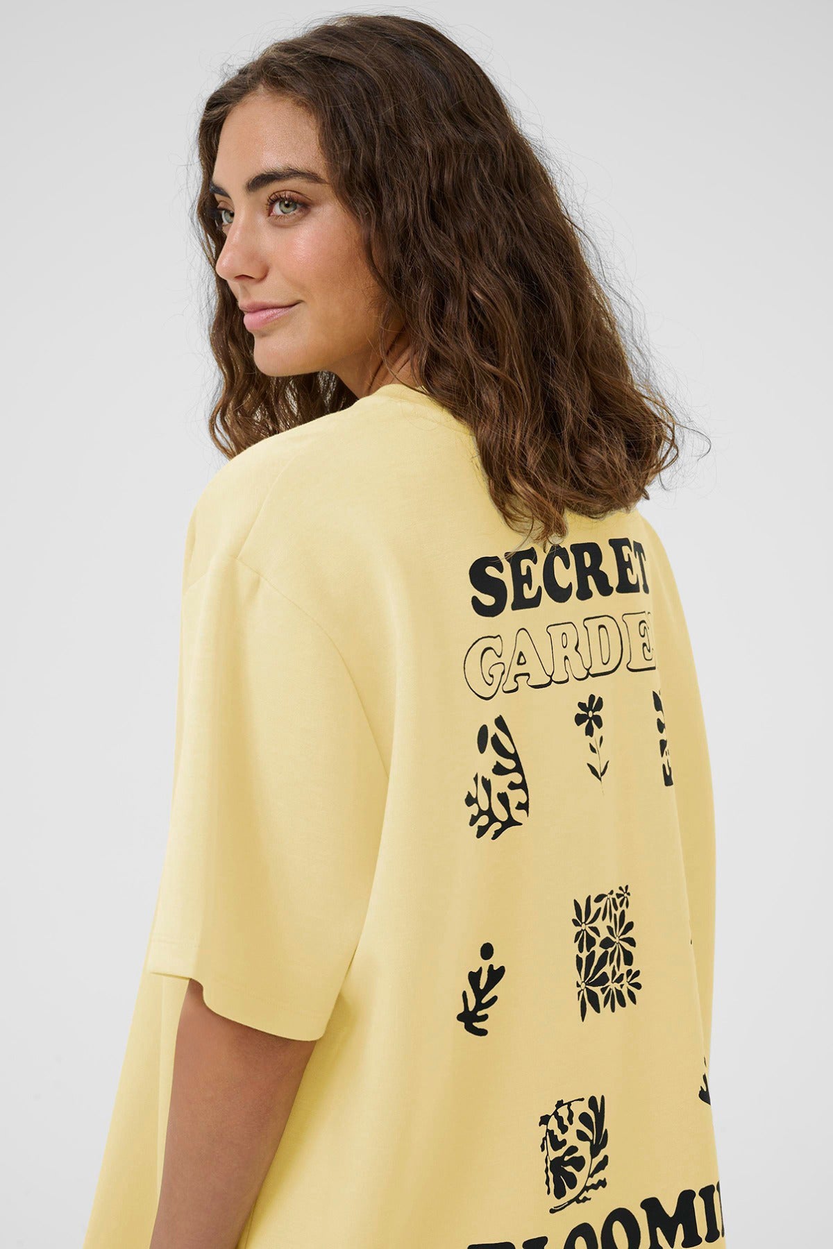 Oversize lemonfarvet t-shirt med sort print og tekst på ryggen, løst fit.