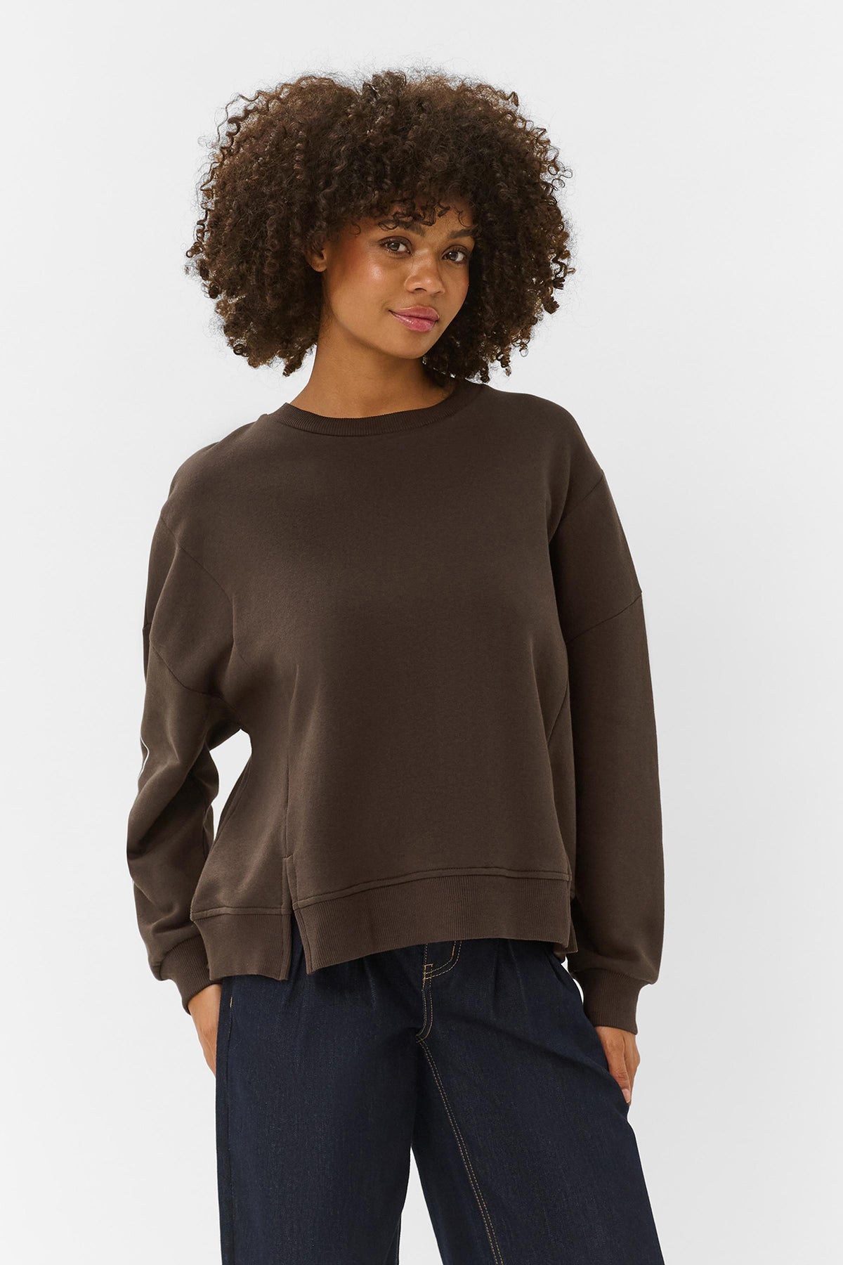 Brun sweatshirt med rund hals og løstsiddende pasform på model med mørkt, krøllet hår.