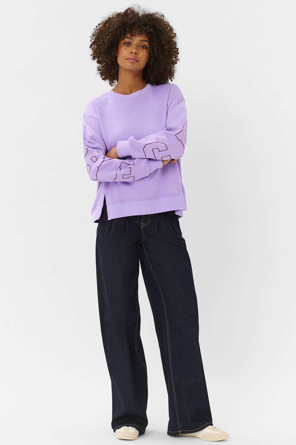 Lilla sweatshirt med rund hals og sort grafik på ærmet, stylet med vidde bukser.