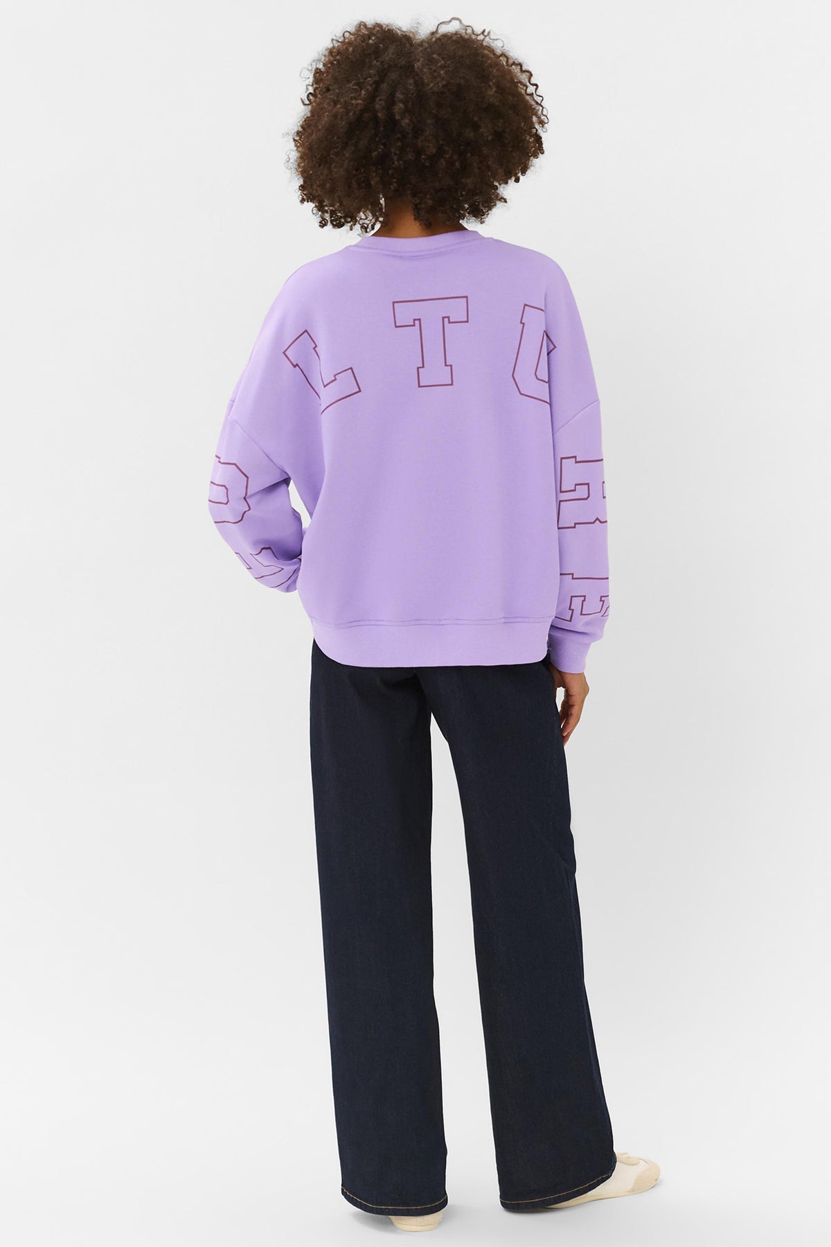 Lilla sweatshirt med stort lommetryk på ryggen og sorte bukser, set bagfra.