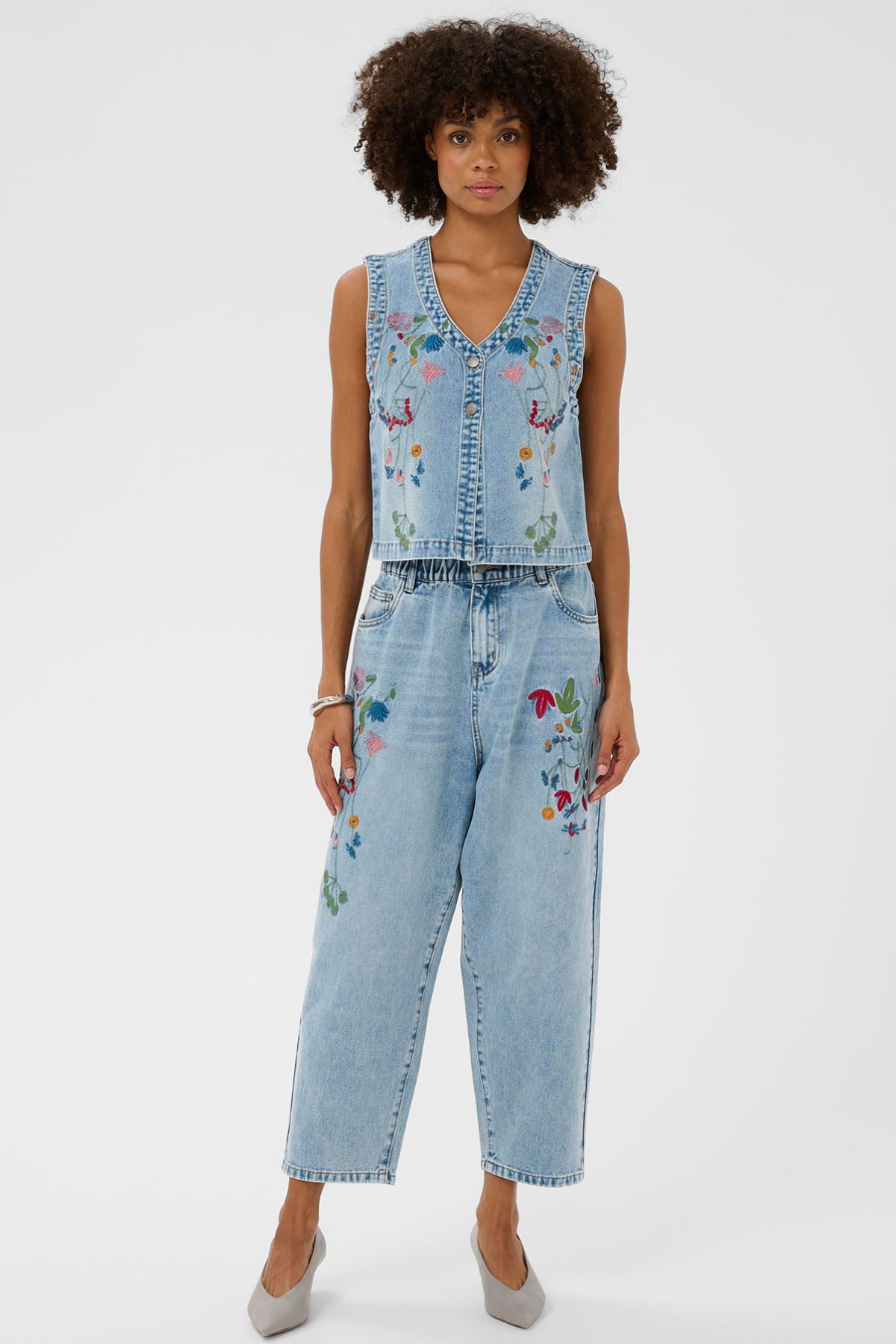 Lysblå denimvest med farverig blomstret broderi, krave og knaplukning, ærmeløs model.