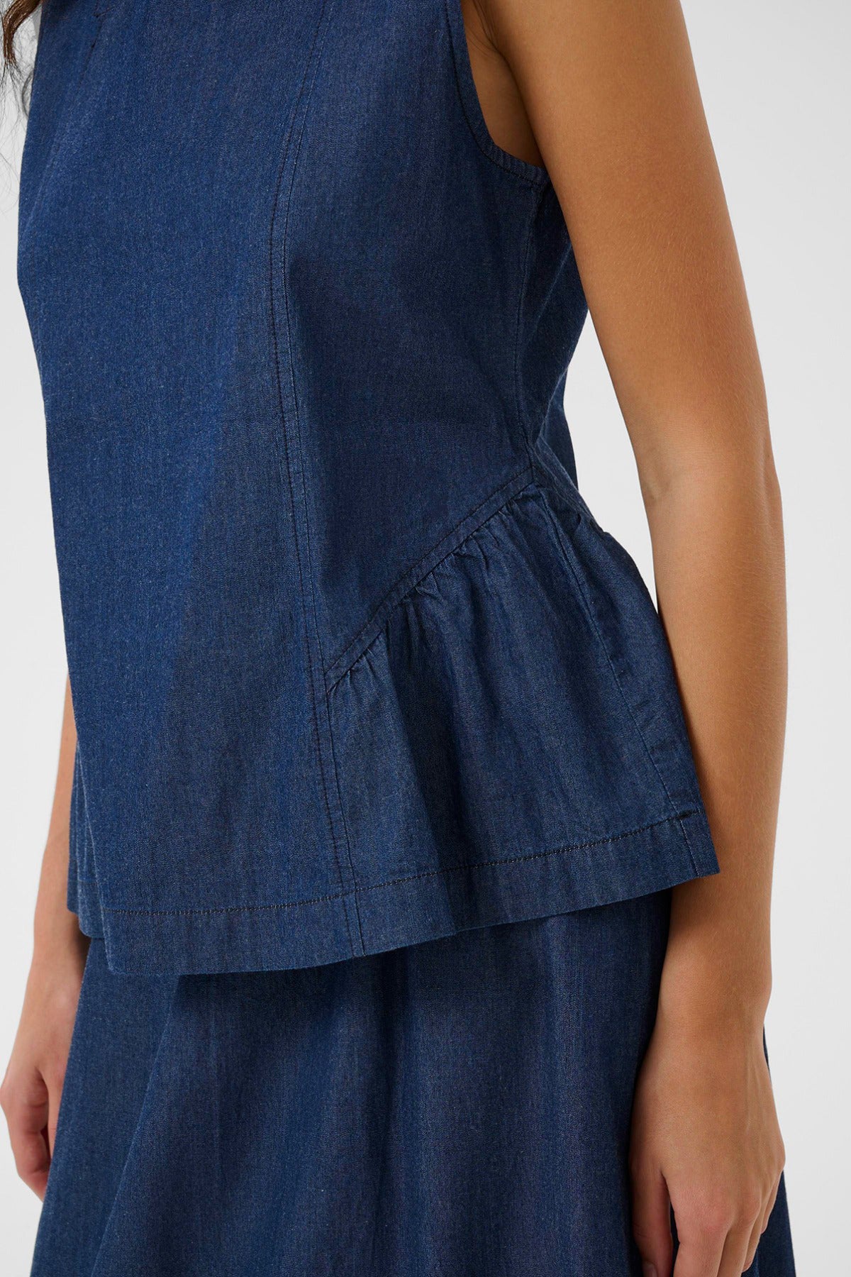 Denim top i mørkeblå med peplum-detalje og rund hals, ærmeløs design.