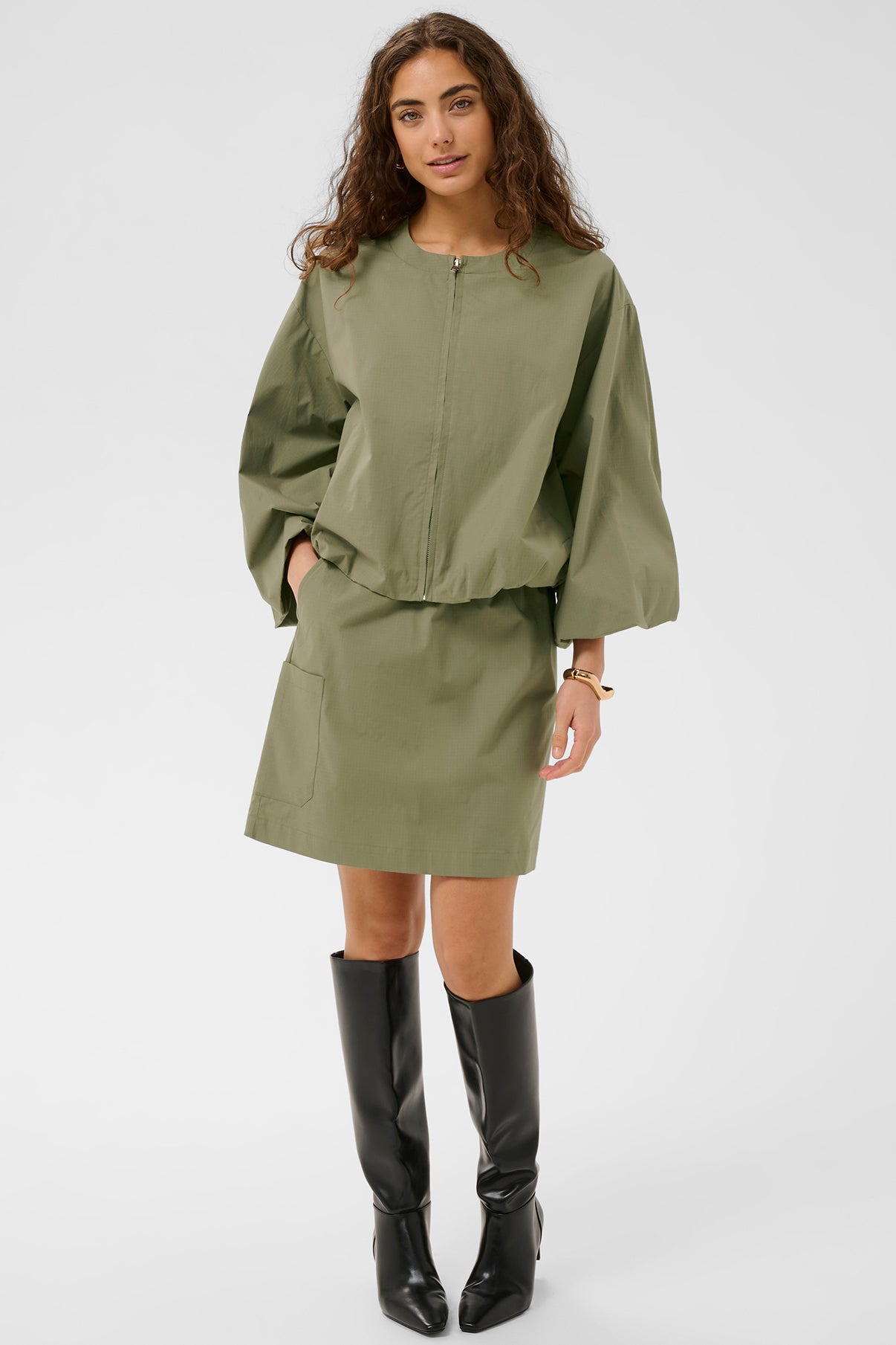 Dusky grøn kort nederdel med lommer og lige pasform, stylet med matchende oversized bluse og sorte knæhøje støvler.