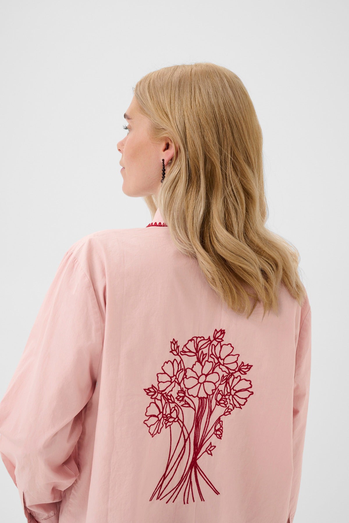 Lyserød skjorte med løstsiddende ærmer og rød blomsterillustration på ryggen.