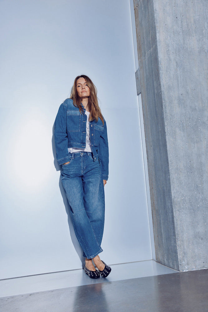 Medium blå højtaljede jeans med barrel fit og afslappet pasform på model, stylet med denimjakke og sorte sandaler.
