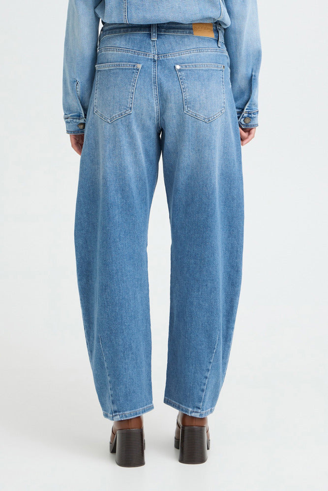 Højtaljede blå jeans med barrel fit og lomme detaljer bagpå, kombineret med en lyseblå skjorte og sorte støvler.