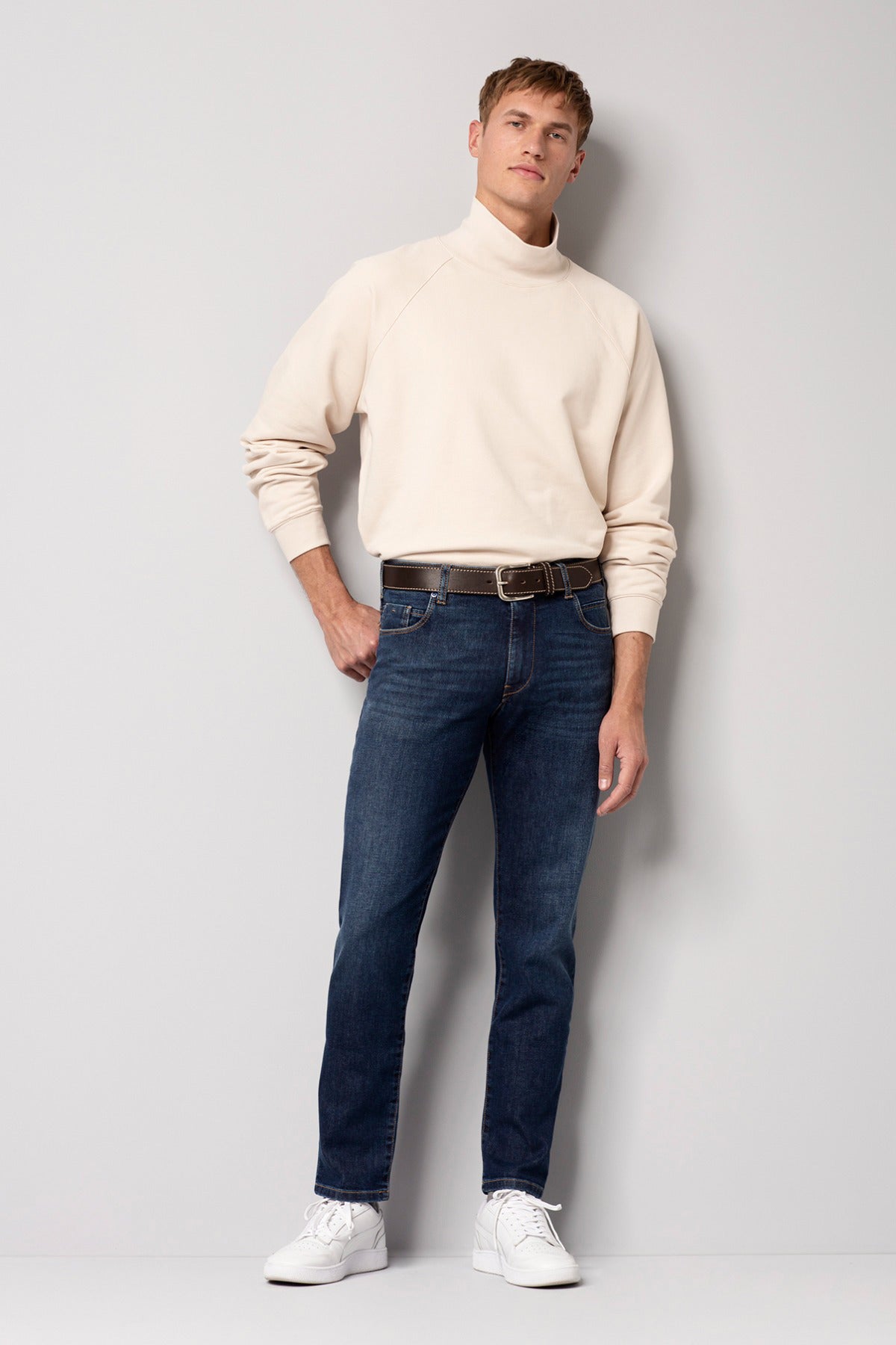 Mørkeblå slim fit jeans med normal talje og let falde, stylet med beige sweatshirt og hvide sneakers.