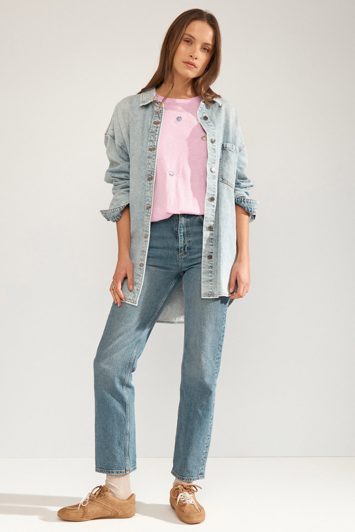 Lyserød T-shirt med broderede muslingedetaljer, rund hals og kort ærme, stylet med blå denimjakke og jeans.