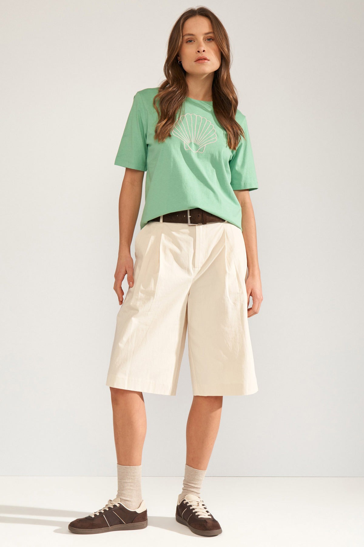 Grøn t-shirt med kort ærme og muslingemotiv på brystet, stylet med lyse bermudashorts.