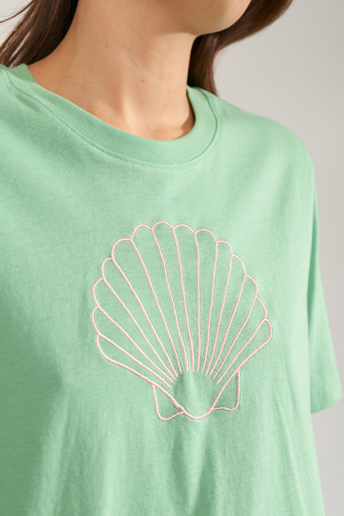 Absintgrøn t-shirt med rund hals og stiliseret muslingetryk i lys kontrast foran.