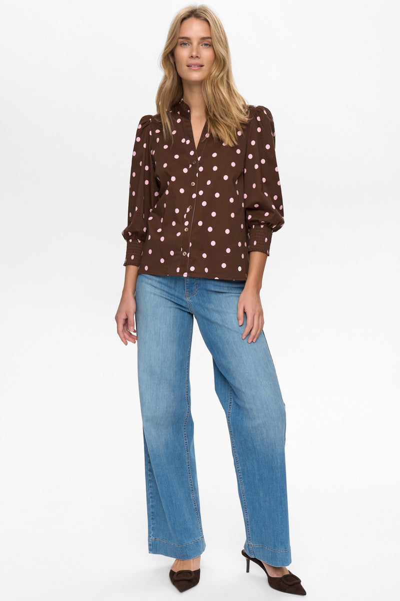 Brun skjorte med hvide prikker og 3/4-ærmer på model, kombineret med lyseblå jeans og sorte hæle.