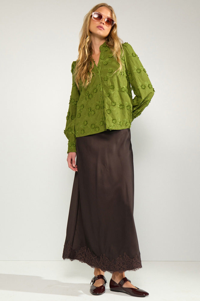 Langærmet grøn bluse med blomsterbroderi og løs pasform, stylet med brun maxi-nederdel og brune sandaler.
