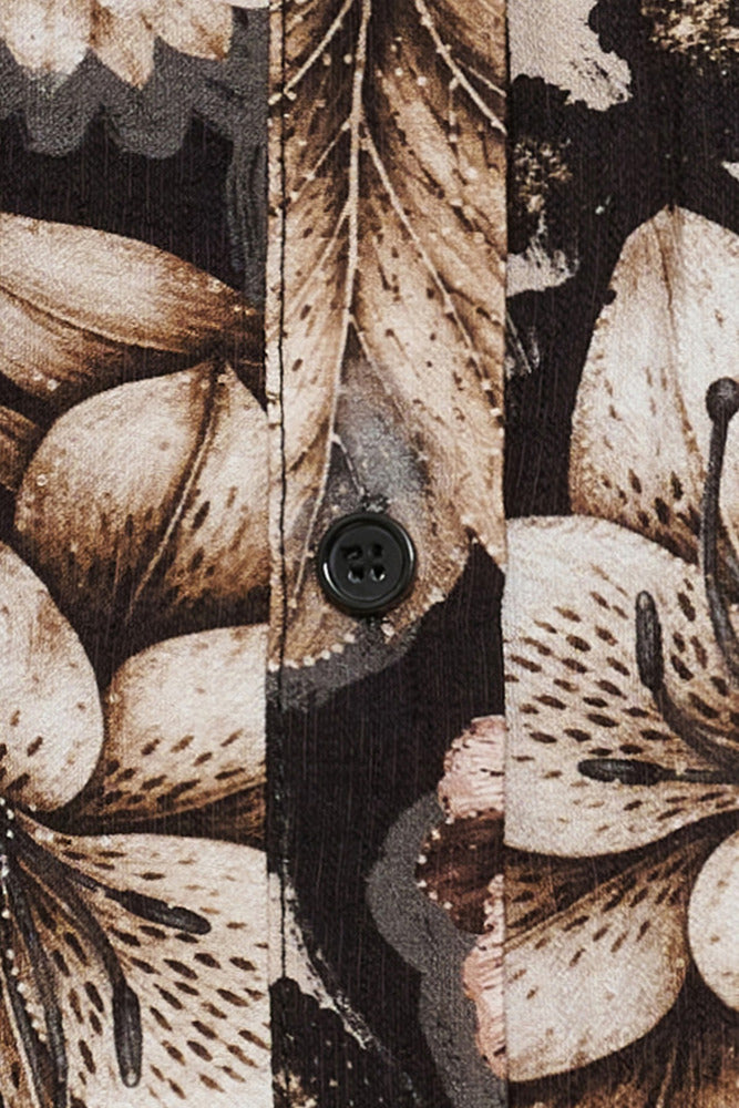 Mønstret skjortebluse med beige og brune blomster og sorte knapper på sort baggrund.