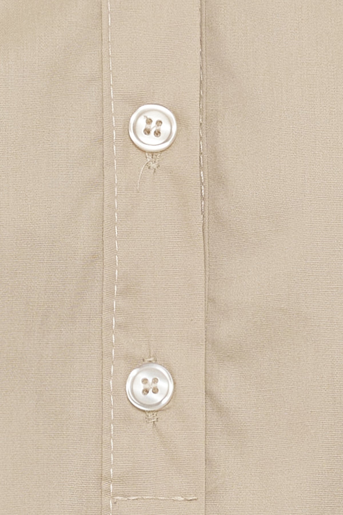 Beige skjortebluse med stolpelukning og perlemorsknapper i close-up.