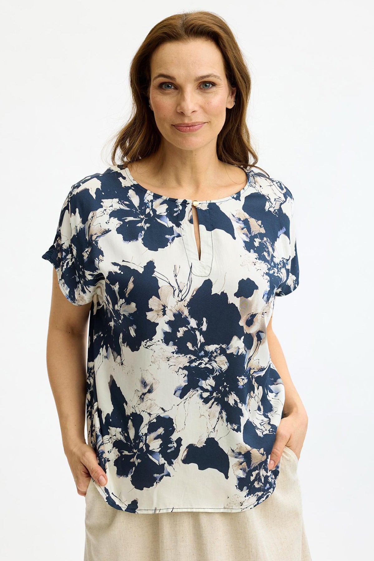 Blå bluse med korte ærmer og blomstret syningsdetalje foran.