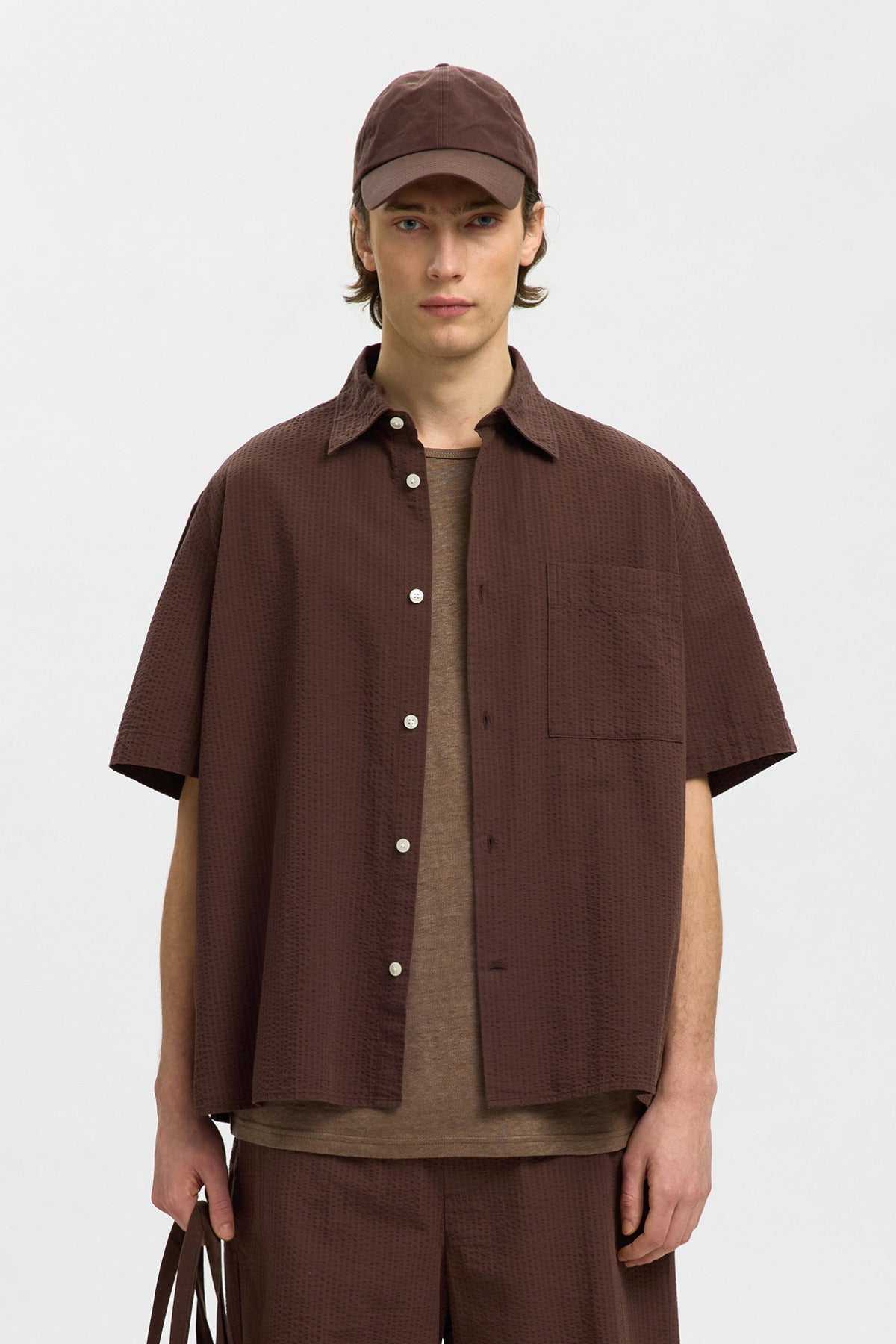 Brun kortærmet skjorte i løs pasform med knapper og brystlomme, båret over beige T-shirt.