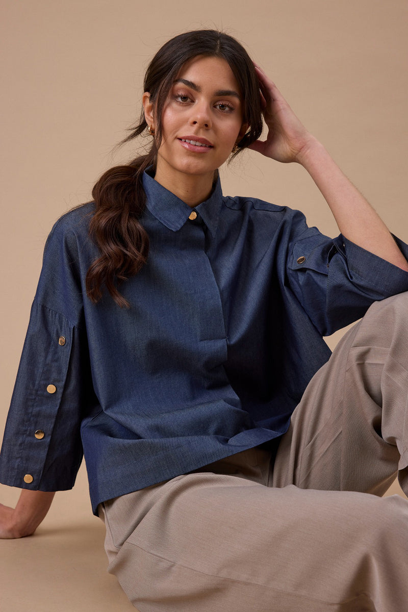 Mid blue denim skjortebluse med trekvartærmer og knapper på ærmer og krave.