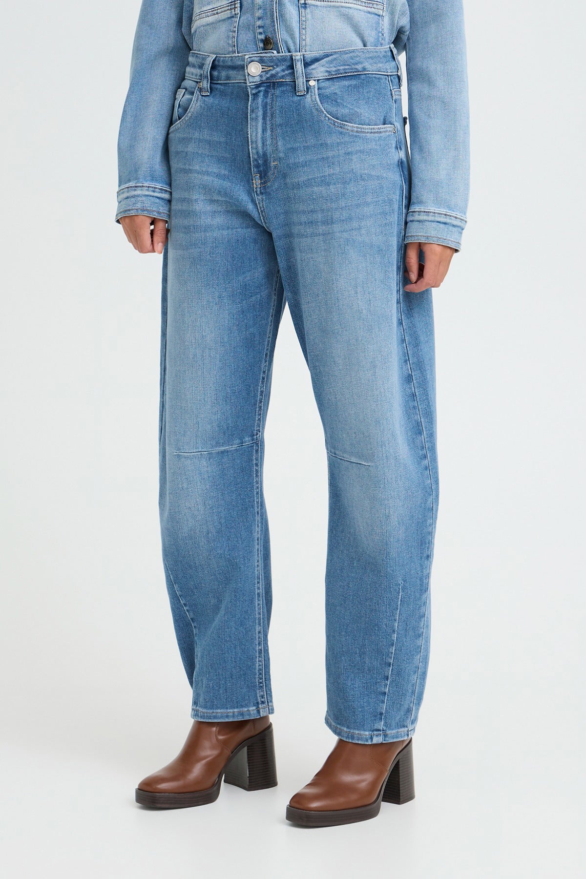 Højtaljede mediumblå jeans med barrel fit og let slidte detaljer, parret med brune støvler.