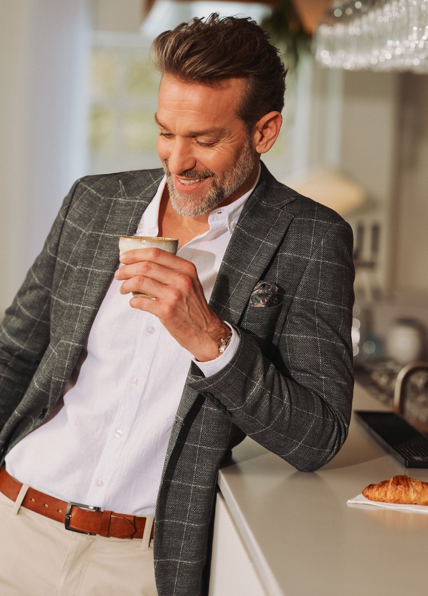 Mand i gråternet blazer og hvid skjorte nyder en kop kaffe i afslappede og stilfulde omgivelser.