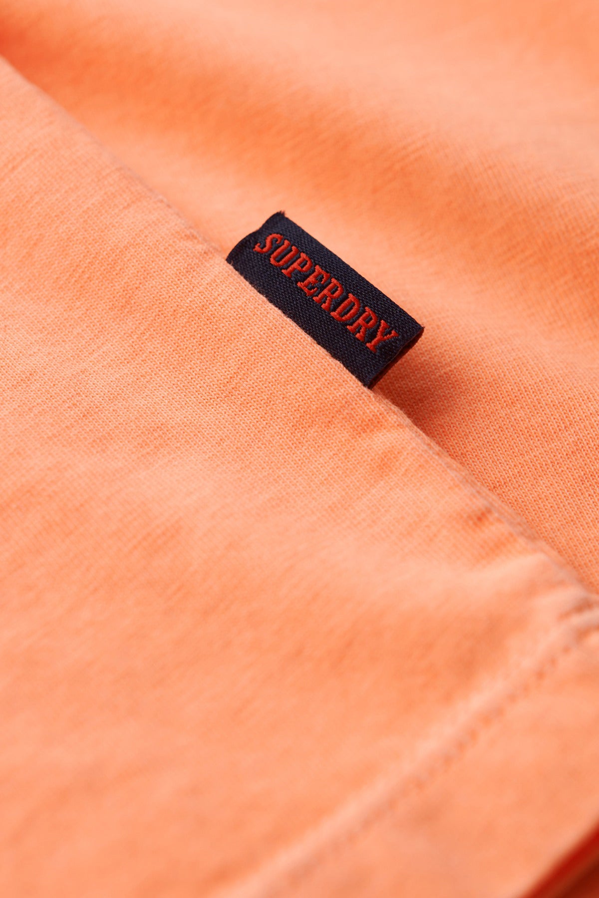 Orange t-shirt med sort og rød Superdry-logo på sømmen.