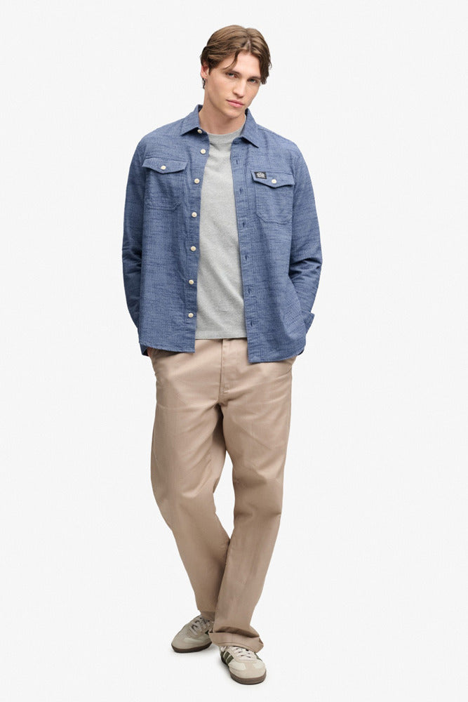 Mand iført flintblå skjorte med v-huls mønster, beige bukser og lyse sneakers.