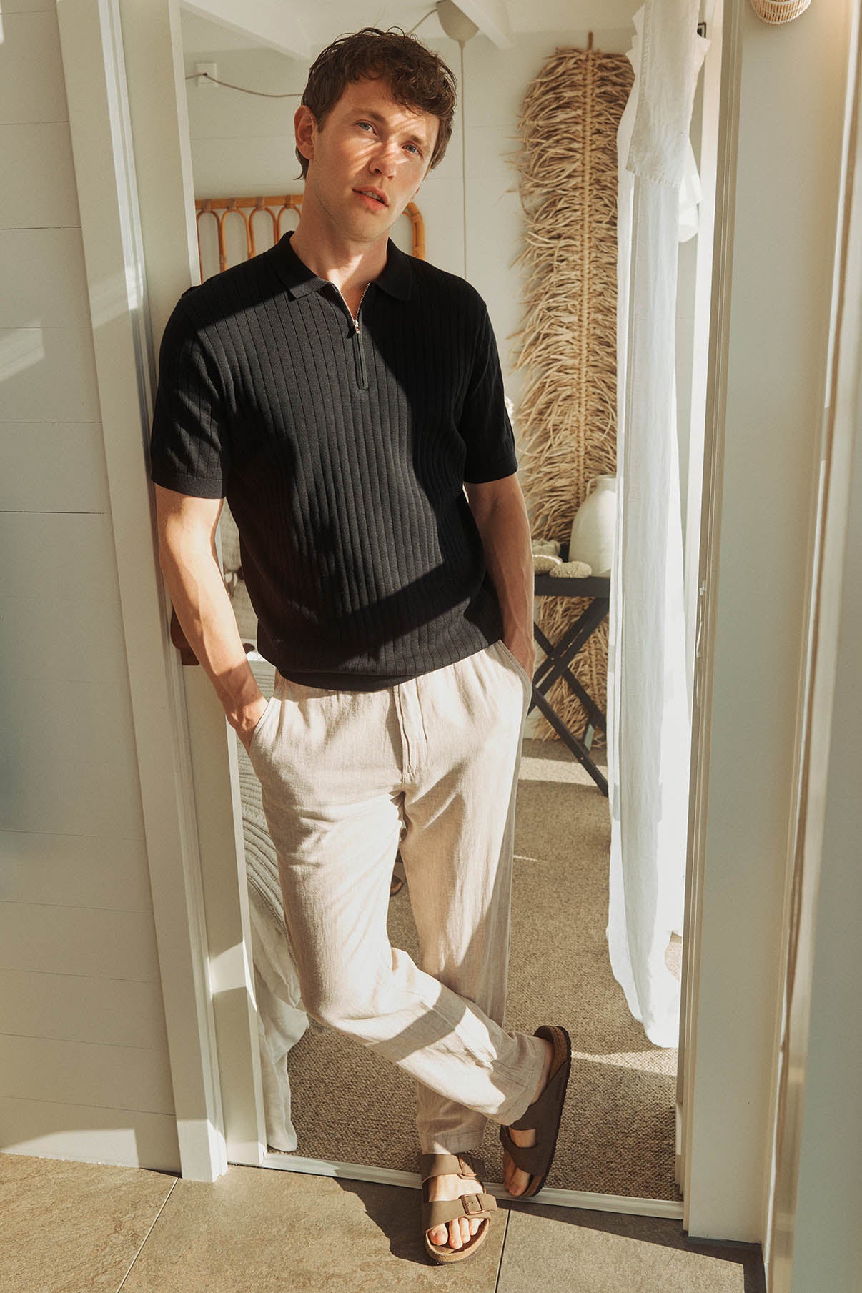 Mand iført lette beige hørbukser med lommer og sort kortærmet striktrøje med lynlås.