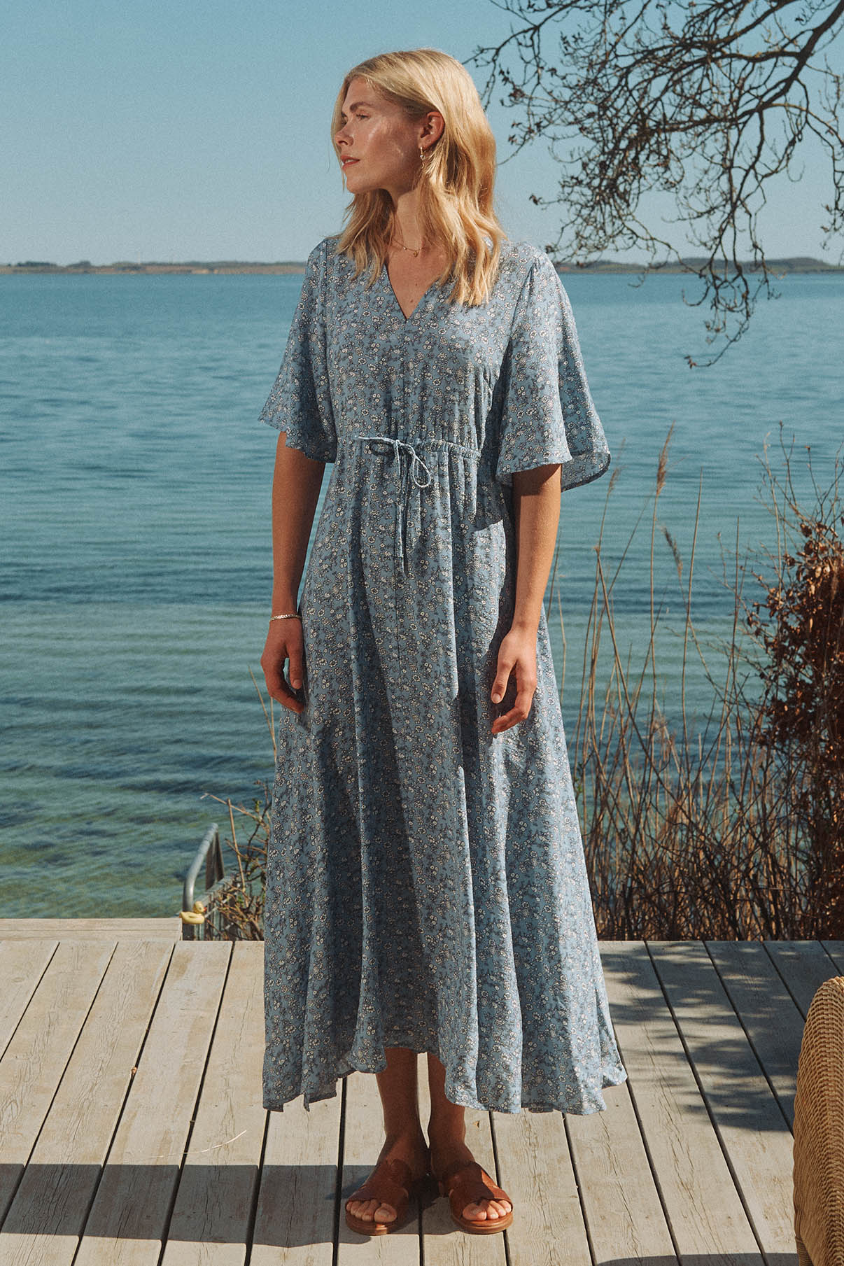 Lang lyseblå kjole med bindebånd, kort ærme og blomsterprint, flowy design.