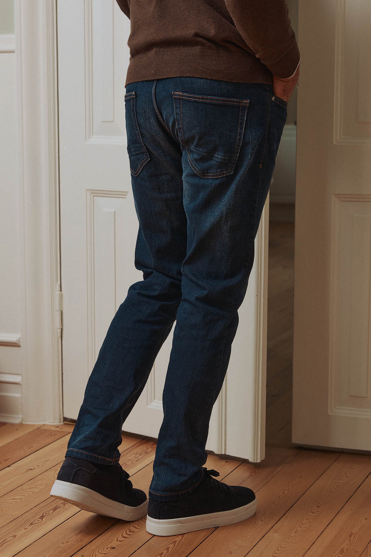 Mørkeblå tapered jeans med baglommer og afslappet pasform, vist bagfra på en model.