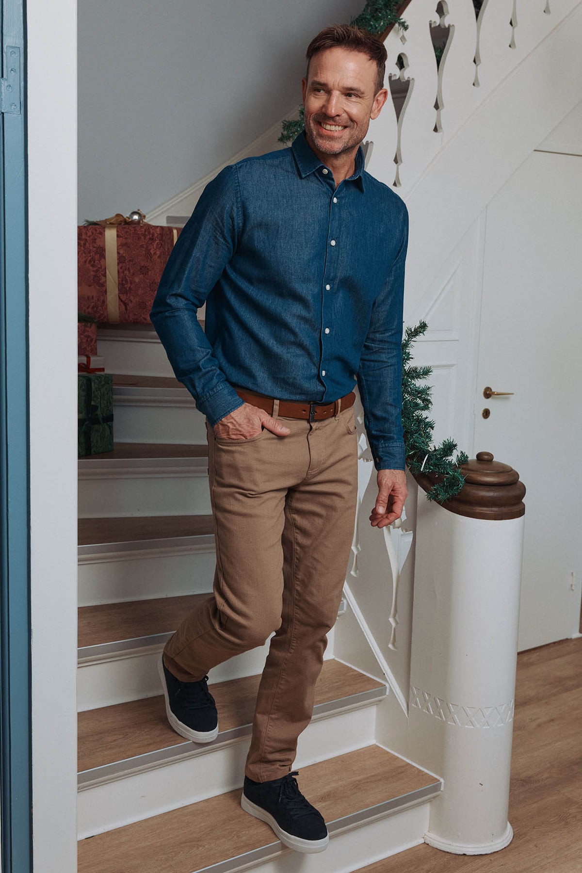 Mand i blå skjorte og beige tapered twillbukser med stræk og sorte sneakers.