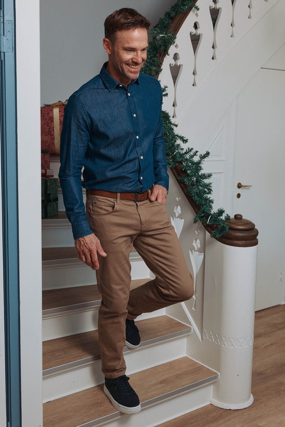 Mand i mørkeblå skjorte og brune tapered twillbukser med stræk og sorte sneakers.